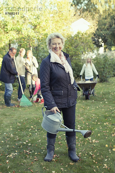 Porträt einer älteren Frau mit Gießkanne bei der Gartenarbeit mit der Familie auf dem Hof.