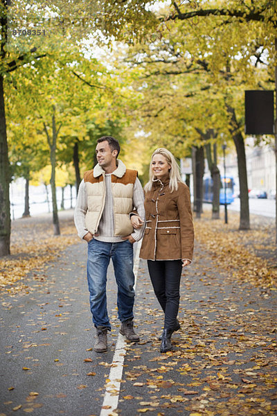 Volle Länge des jungen Paares  das im Herbst auf der Straße läuft.