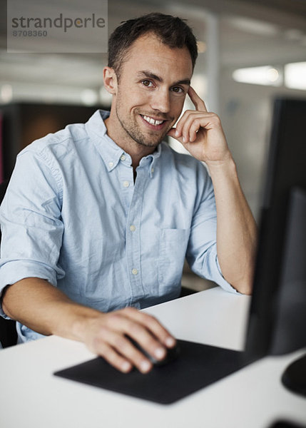 Porträt eines lächelnden Geschäftsmannes mit Computer im Büro