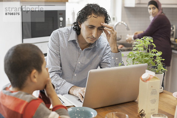Muslimischer Mann bei der Arbeit am Laptop mit Familie in der Küche