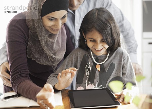 Muslimisches Paar mit Tochter  das zu Hause ein digitales Tablett benutzt