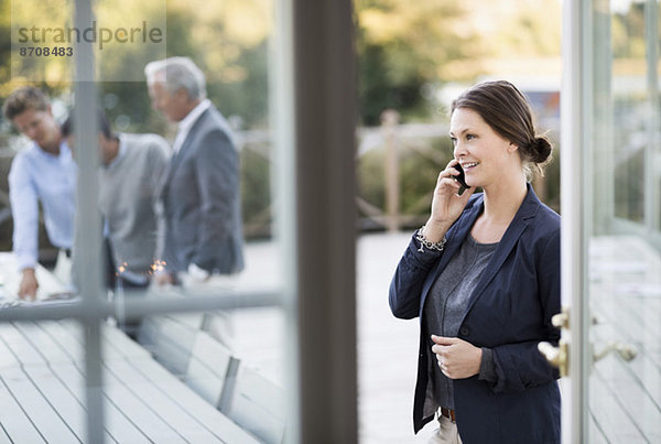Geschäftsfrau mit Handy auf der Terrasse mit Kollegen im Hintergrund