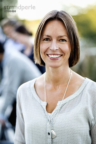 Porträt einer selbstbewussten Geschäftsfrau auf der Terrasse mit Kollegen im Hintergrund