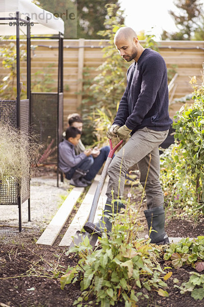 Mann beim Graben im Garten mit Kindern im Hintergrund