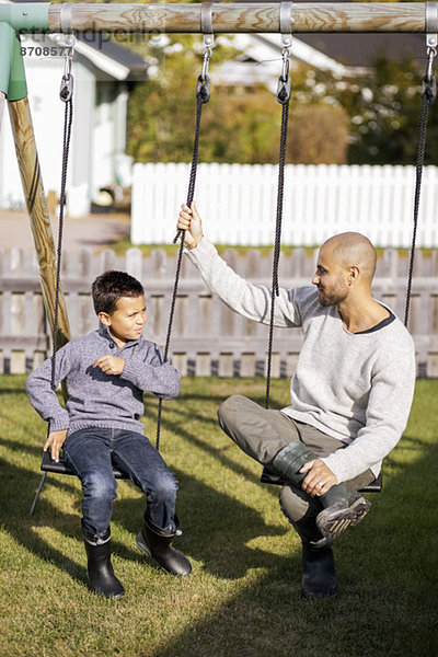 Vater und Sohn sitzen auf Schaukeln im Garten