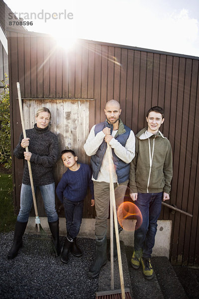 Porträt einer selbstbewussten Familie mit Gartengeräten am Haus