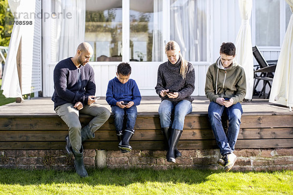 Vierköpfige Familie mit Mobiltelefonen auf dem Hof