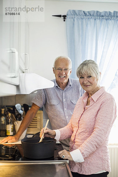 Porträt eines glücklichen Seniorenpaares beim Kochen am Küchentisch