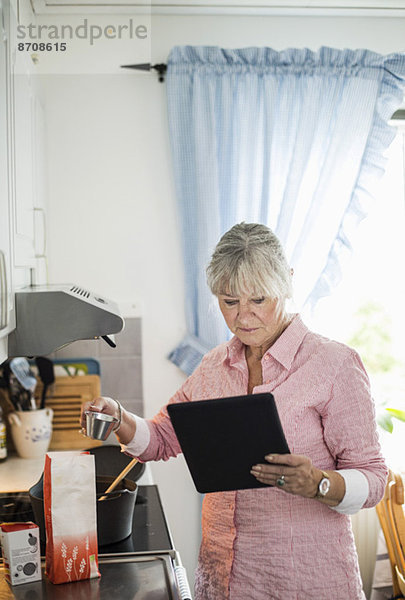 Seniorin beim Kochen  während sie sich das Rezept auf einem digitalen Tablett ansieht.