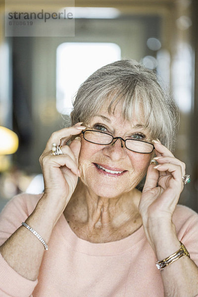 Porträt einer älteren Frau  die im Haus lächelt und eine Brille trägt.