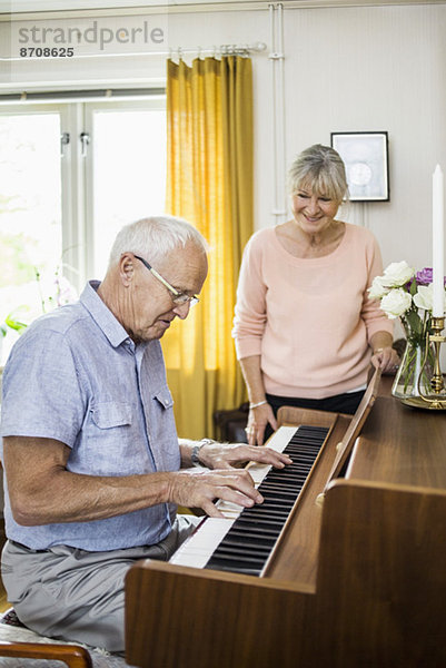 Ein älterer Mann spielt Klavier  während eine Frau ihn drinnen ansieht.
