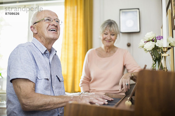 Glücklicher älterer Mann  der Klavier spielt  während er mit einer Frau im Haus sitzt.