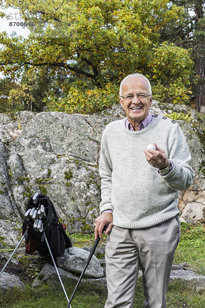 Porträt eines glücklichen älteren Mannes mit Golfball und Schläger im Hof