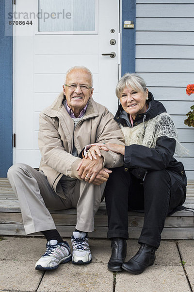 Porträt eines lächelnden älteren Paares  das auf der Veranda sitzt.