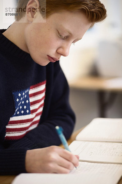 Highschool-Junge schreibt am Schreibtisch im Klassenzimmer