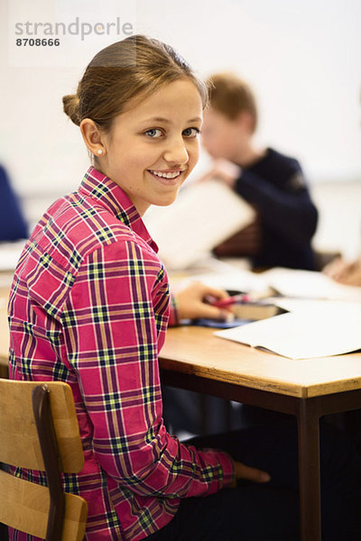 Porträt einer fröhlichen Schülerin am Schreibtisch im Klassenzimmer