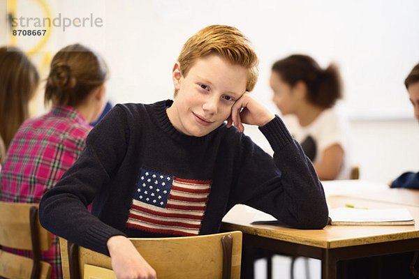 Porträt eines selbstbewussten Schülers am Schreibtisch im Klassenzimmer