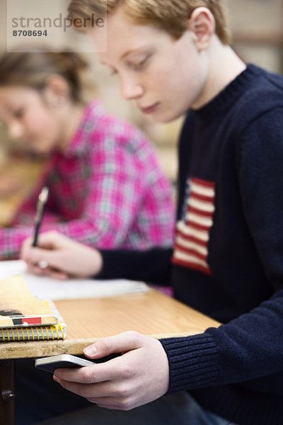 High-School-Junge mit Smartphone beim Lernen im Klassenzimmer