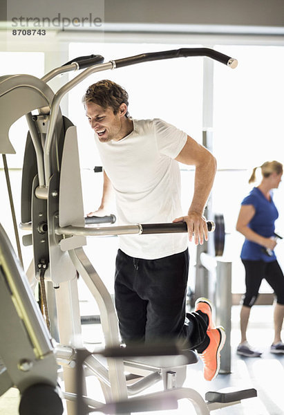 Mann trainiert an der Klimmzugmaschine im Fitnessstudio
