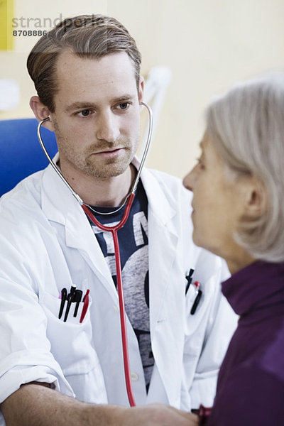 Männlicher Arzt untersucht das Herz der älteren Frau mit Stethoskop in der Klinik