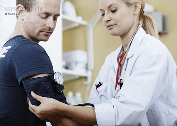 Ärztin wickelt die Manschette an den Arm des Patienten  bevor sie den Blutdruck in der Klinik nimmt.