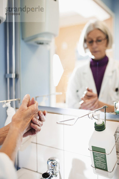 Abgeschnittenes Bild einer Oberärztin  die sich die Hände im Krankenhausbad wäscht.
