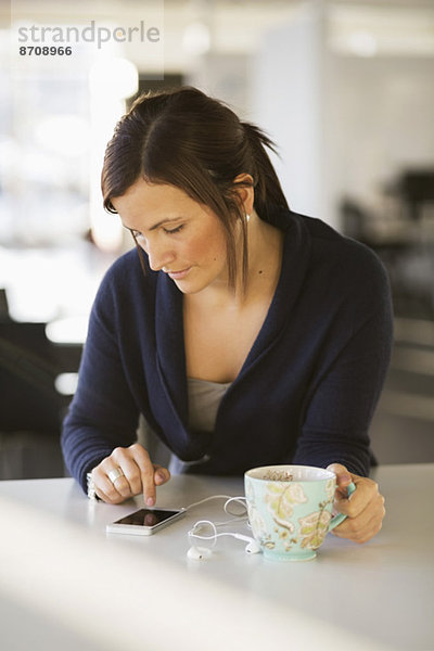 Geschäftsfrau mit Smartphone beim Kaffeetrinken im Büro