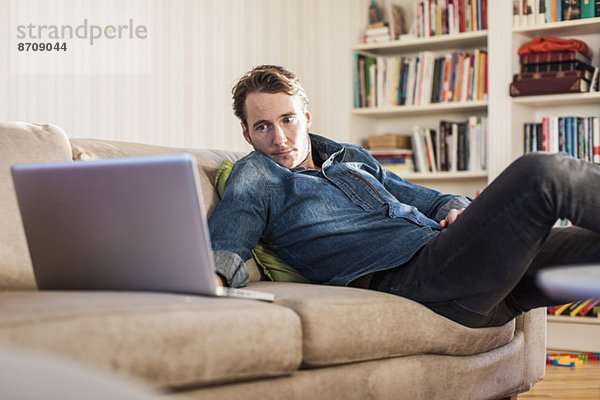 Mann mit Laptop auf Sofa im Wohnzimmer