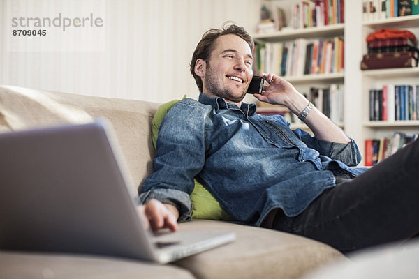 Mann auf Abruf während der Benutzung des Laptops auf dem Sofa zu Hause