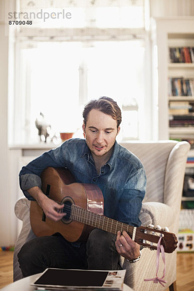 Mittlerer Erwachsener Mann  der zu Hause Gitarre spielt