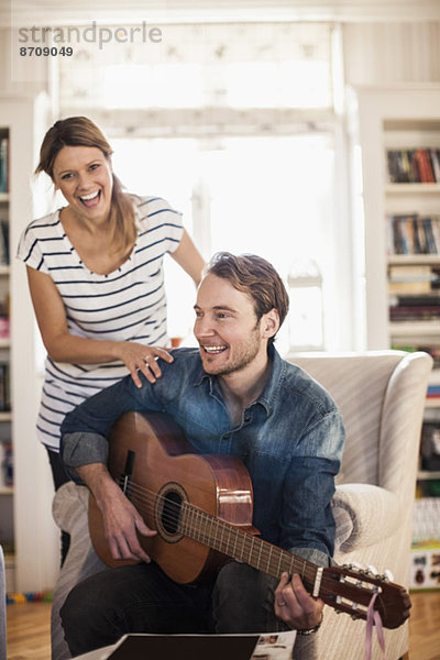 Glücklicher Mann spielt Gitarre für Frau im Haus