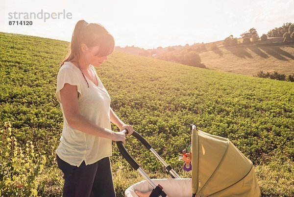 Mutter schlendert durch die Landschaft und schiebt den Kinderwagen.