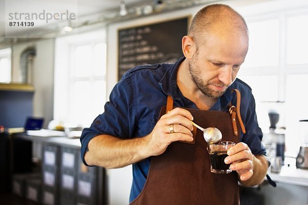 Männlicher Barista  der das Kaffeeglas in der Kaffeebar rührt