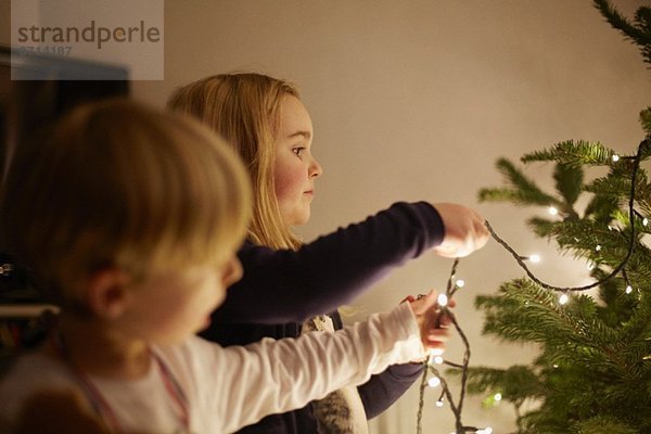 Junge Geschwister beim Aufstellen von Weihnachtslichtern