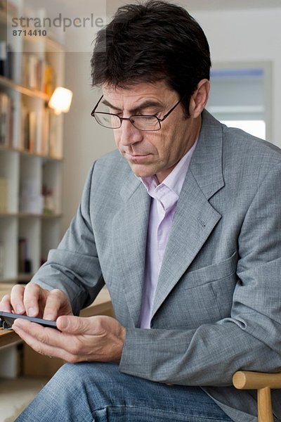 Älterer Mann  der zu Hause arbeitet und auf dem Handy SMS schreibt