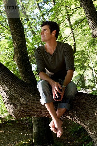 Erwachsener Mann sitzt auf einem Baumstamm im Wald