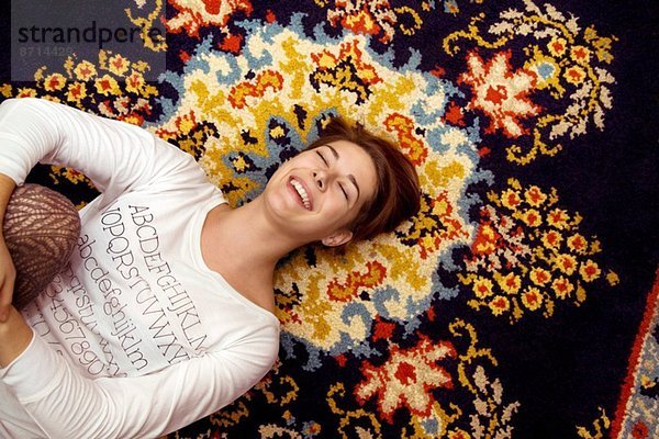 Junge Frau auf gemustertem Teppich liegend lachend