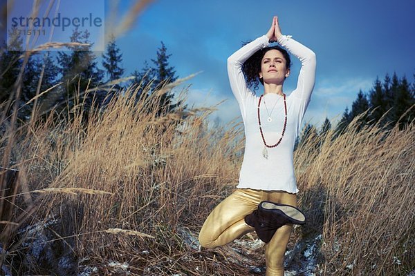 Mittlere erwachsene Frau macht stehende Baum-Yoga-Pose im Wald