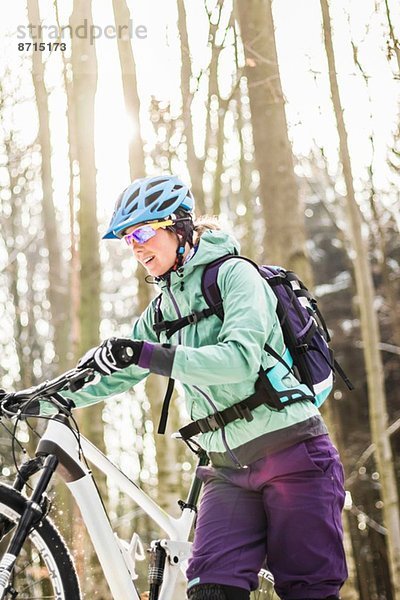Mittlere erwachsene Mountainbikefahrerin  die das Fahrrad durch den Wald schiebt