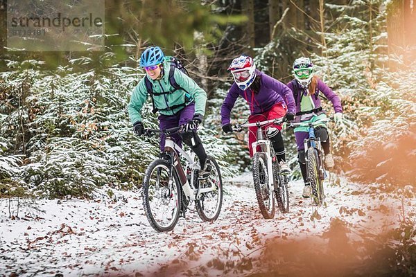 Drei Mountainbikerinnen fahren durch den Wald im Schnee