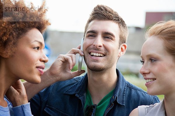 Drei junge erwachsene Freunde  einer spricht mit einem Smartphone