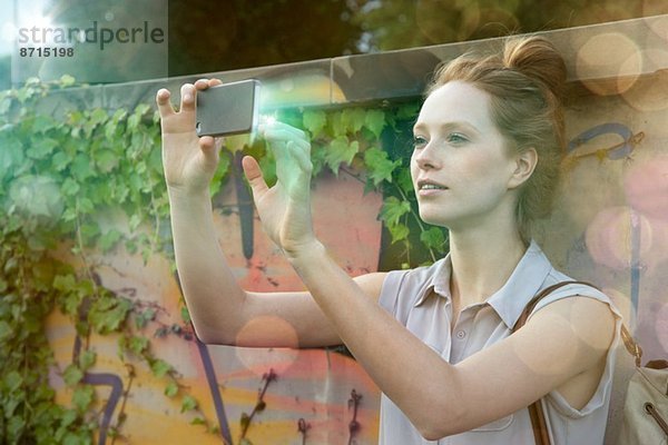 Junge Frau fotografiert sich selbst auf beleuchtetem Smartphone