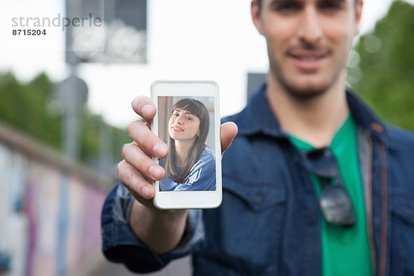 Junger Mann hält Smartphone mit Foto der Freundin in der Hand