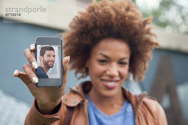 Junge Frau hält Smartphone mit Foto des Freundes hoch