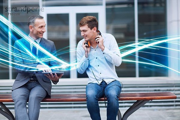 Geschäftsmann und junger Mann beim Betrachten des digitalen Tabletts und der Wellen des blauen Lichts