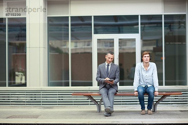 Geschäftsmann und junger Mann sitzend auf der Bahnhofsbank