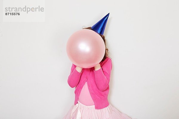 Mädchen hält rosa Ballon vor dem Gesicht
