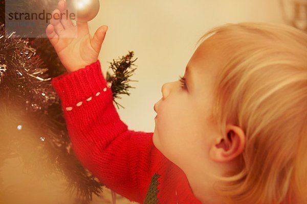 Kleines Mädchen schaut auf Weihnachtskugel