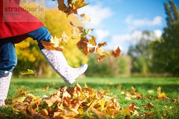 Ausgeschnittene Aufnahme einer reifen Frau  die Herbstblätter im Park kickt.