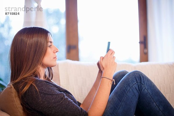 Junge Frau mit Handy auf dem Sofa